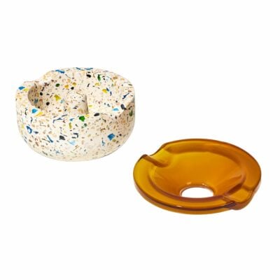 The NWTN Home Symi Ashtray comes in two styles: one with colorful terrazzo-like speckles, and another in smooth translucent amber brown. Each has notches for holding cigarettes and adds a stylish accent to your decor.