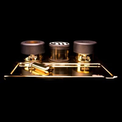 The 24k Stashtray Bundle is a gold and black smoking accessory set featuring two containers, an M logo grinder, a tray, and a rolling tool—all showcased against a sleek black background.
