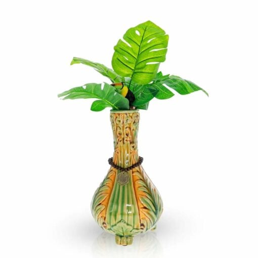 The TocaCabana Vase Bong features green and brown leaf patterns, tropical artificial green leaves, a yellow and black bird figurine perched among them, plus a coin and rope accent around the neck for added charm.