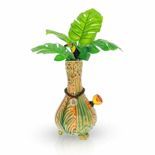 The TocaCabana Vase Bong features a tropical vase design with green leaves, a toucan figurine on top, orange and green patterns on the body, and a circular pendant hanging around its neck.