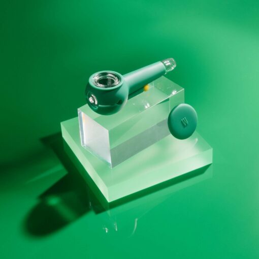 The Pipe - Forest, a modern forest-green smoking pipe with a glass bowl, rests on a clear rectangular acrylic stand beside its matching green lid, all displayed against a vibrant green background.