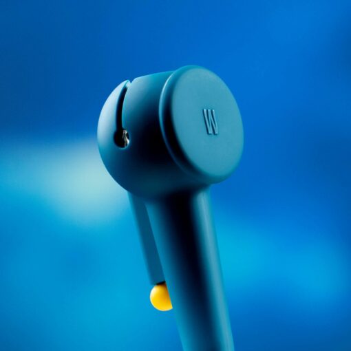 A close-up of The Pipe - Midnight wireless earbud, featuring a blue body with a circular top bearing a W logo. The background is a smooth midnight blue gradient, with a small yellow accent at the bottom of the earbud.