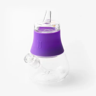 The Bubbler - Grape is a clear glass bubbler with a rounded base and short, bent mouthpiece. It features a bright grape-purple silicone sleeve for grip and is shown against a plain white background.