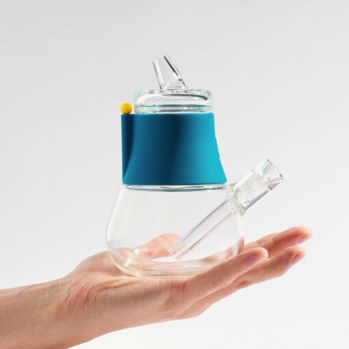 A hand holds The Pipe - Hot Pink, a modern clear glass teapot featuring a vibrant hot pink silicone band and an angled spout and lid, set against a plain white background.