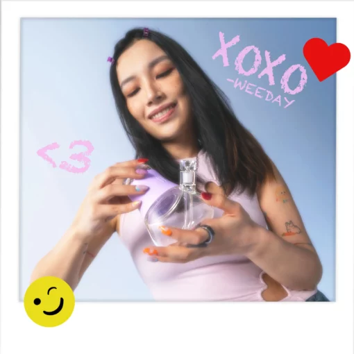 A smiling woman with long hair in a light purple top holds a round bottle. Playful doodles surround her, and text reads XOXO - WEEDAY. The scene glows with the soft hues of The Iridescent Bubbler - Lavender.