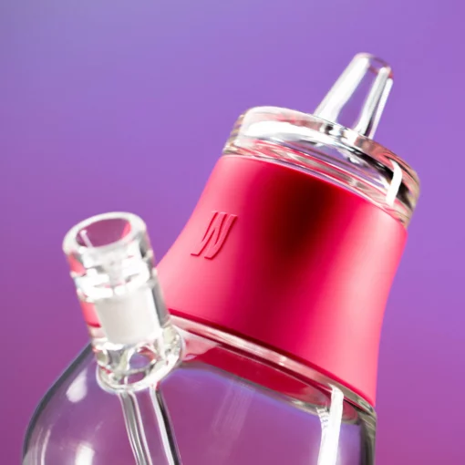 The Bubbler - Hot Pink features clear, smooth glass with a bold hot pink silicone collar and an embossed “W” logo. This sleek smoking accessory is shown close-up against a purple background.