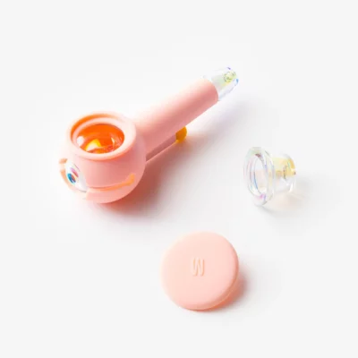 The Pipe Iridescent - Bubblegum features a pastel pink body, clear glass bowl, matching pink lid, and a small clear accent, all shown on a white background.
