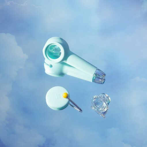 The Pipe Iridescent - Sky is displayed with pale blue and clear medical devices, including a handheld round device, a circular item with a pin, and a clear plastic cap, all floating against a soft iridescent sky background.