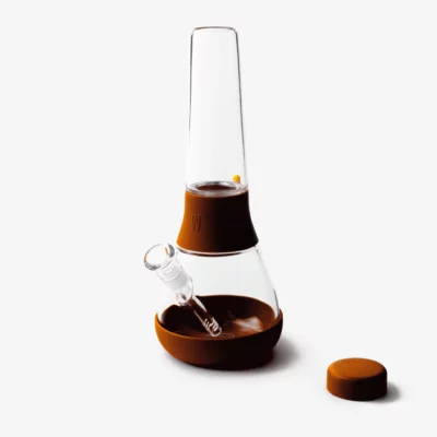The Bong - Leather is a modern brown and clear glass water pipe with a removable mouthpiece, separate round cap, and leather accents, shown on a white background.