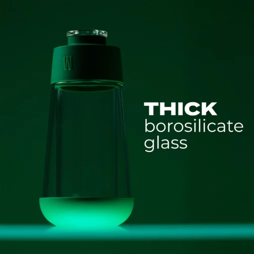 The Gravity Bong - Forest features a thick borosilicate glass bottle with a green cap, illuminated from below against a deep green, forest-inspired backdrop. "THICK borosilicate glass" is highlighted—ideal for your next gravity bong session.
