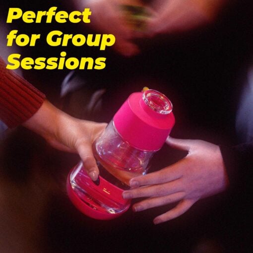Two hands exchange The Gravity Bong - Hot Pink, with "Perfect for Group Sessions" in bold yellow above. A blurred background emphasizes the hands and this stylish hot pink bong.