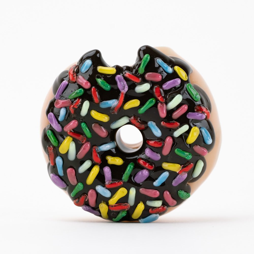 The Empire Glassworks Donut Bite Me Dry Pipe is a round donut-shaped dry pipe with chocolate glaze and colorful sprinkles, featuring a small bite on the top left edge, shown against a plain white background.