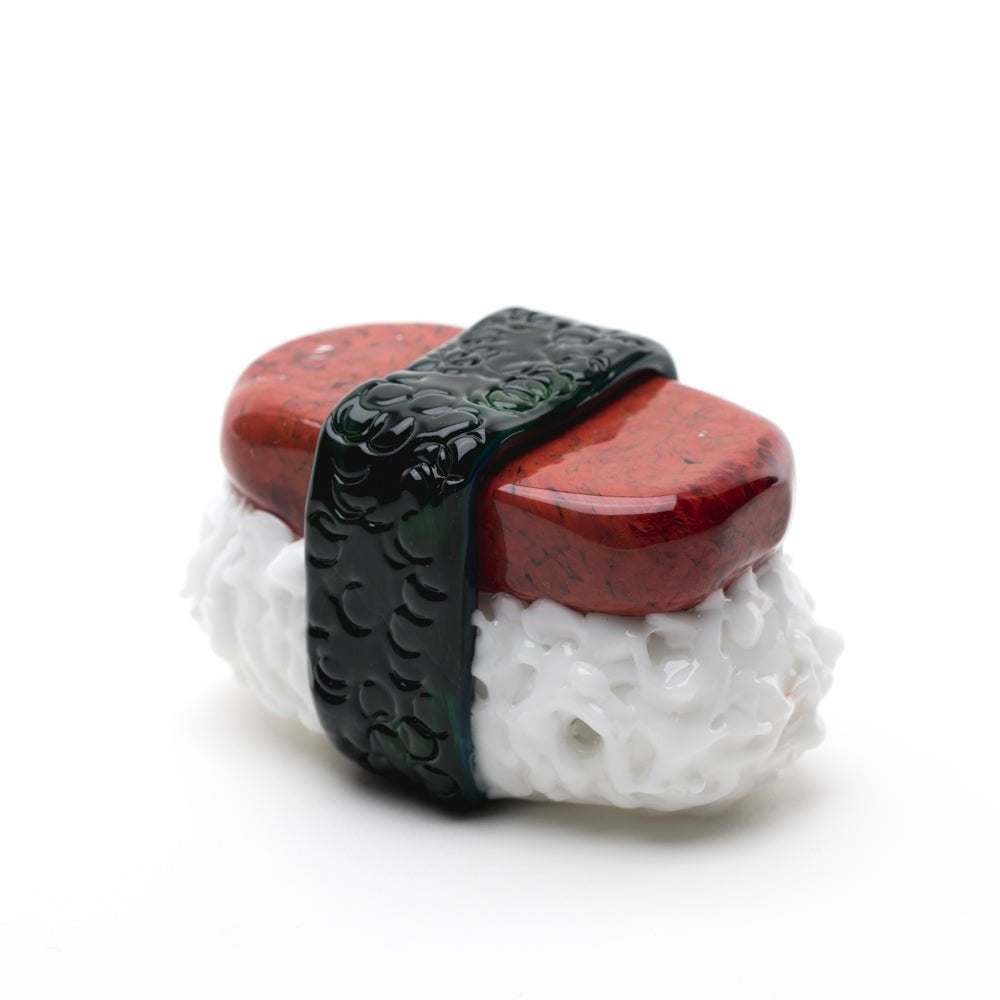 The Empire Glassworks Spam Musubi Dry Pipe features a realistic white rice base, glossy red top, and black seaweed strip—crafted from glass or ceramic and displayed on a white background.