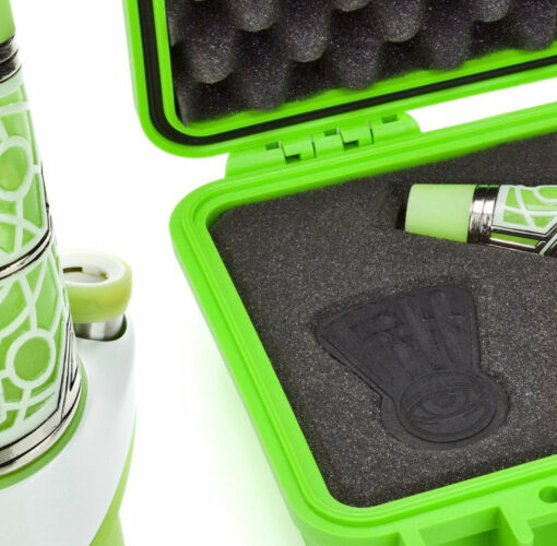 A close-up of the Ryan Fitt Neon Puffco Peak Complete Set, featuring its green and white patterned cylinder beside an open foam-lined case with a matching piece secured in a cutout slot.