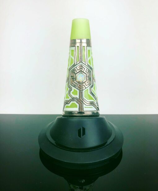 The Ryan Fitt Neon Puffco Peak Complete Set features a decorative cone with a green geometric pattern and metallic accents, standing upright on a black circular base, displayed against a plain white background.
