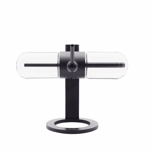 A modern, minimalist table lamp inspired by the Stündenglass Gravity Infuser, featuring a cylindrical glass shade, black metal base with horizontal tube design and round open base, set against a white background.