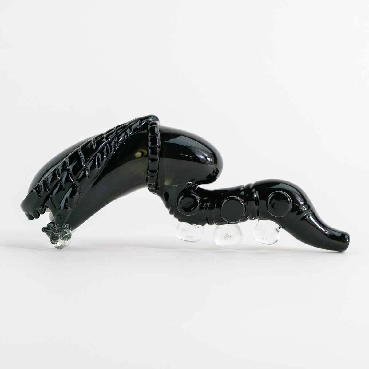 Empire Glassworks Alien Hand Pipe featuring a sculpted alien design with black glass body, white teeth details, and glow-in-the-dark beads.