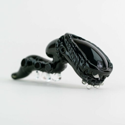 Empire Glassworks Alien Hand Pipe featuring a sculpted alien design with black glass body, white teeth details, and glow-in-the-dark beads.
